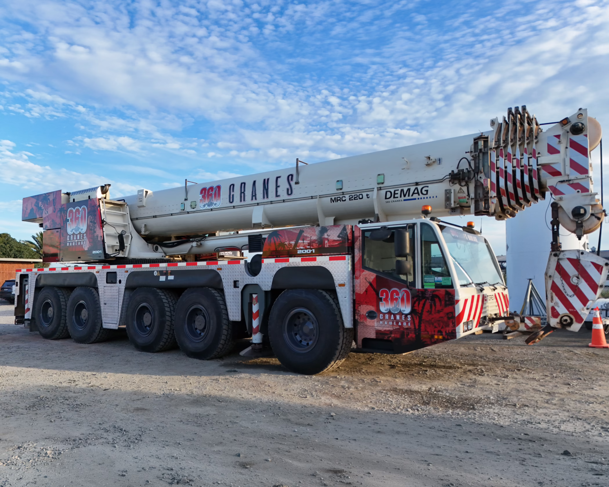A large white five-axle Demag all-terrain mobile crane parked on a gravel lot, featuring custom red and black "360 Cranes" branding on the cab and main boom.